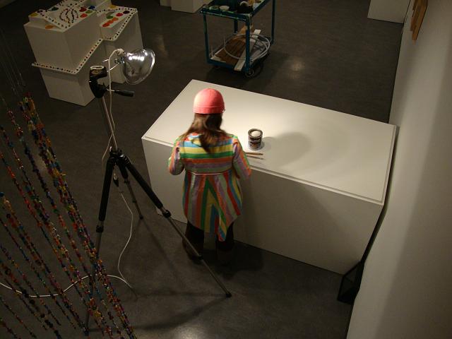 install - playing in the rainbow (33).JPG - lara coating the top of the big plinth with clear varnish. the regular gallery mat paint did not make it easy to move the disks around and also marked easily - the varnish provided a much better surface to "play" on.